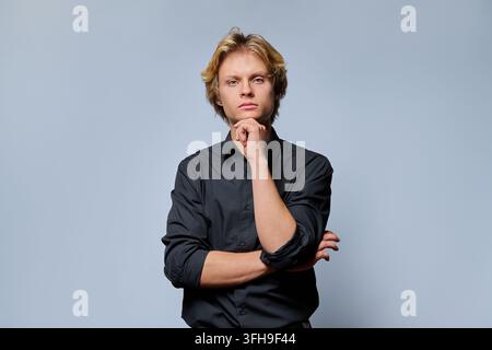 Thoughtful young man touching chin looking at camera against light studio background Stock Photo