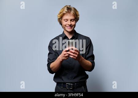 Smiling young man holding smartphone and texting in studio portrait Stock Photo