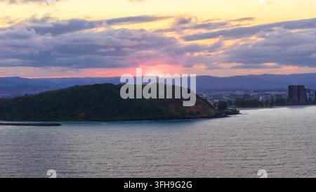 Aerial view of the headland at sunset with calm ocean waters, lush vegetation on the hill, and a vibrant sky over Burleigh Heads, Queensland, Australi Stock Photo