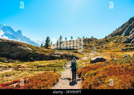 Scenic alpine landscape of solo female hiker with backpack standing on mountain ridge looking at Mont Blanc massif rocky peak and autumn forest under Stock Photo