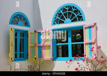 A colorful seaside house facade with turquoise windows, arched glass fanlights, open pastel shutters, and flowering bougainvillea creating cheerful ex Stock Photo