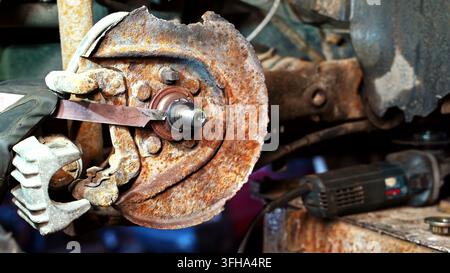 View of a mechanic using a tool on a heavily rusted car brake rotor and hub assembly in a workshop in Latvia. Stock Photo