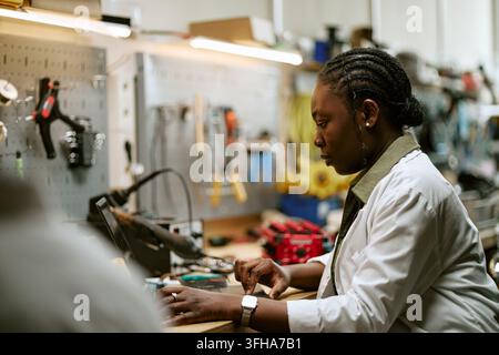 Focused Black Woman Engineer Working on Laptop in Workshop Stock Photo