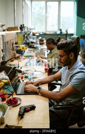 Indian Engineer Typing on Laptop in Hardware Workshop Stock Photo