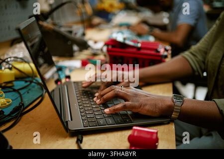 Black Woman Typing on Laptop in Electronics Workshop Stock Photo