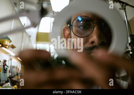 Portrait of Indian Man Inspecting Electronics with Magnifier Stock Photo