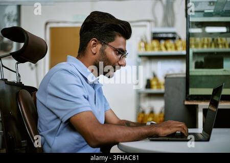 Indian Man Typing on Laptop Computer While Working in Modern Office Stock Photo