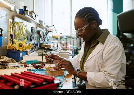 Black Female Engineer Soldering Circuit Board in Robotics Lab Stock Photo