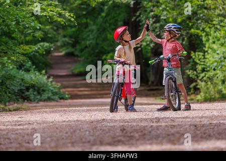 Children boy and girl high-fiving beside bicycles in the forest Stock Photo