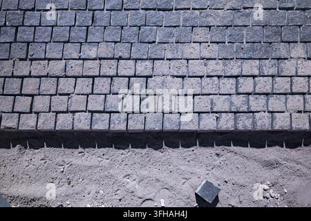 High angle view of granite cobblestone blocks being laid on a sand foundation during sidewalk construction outdoors. Stock Photo