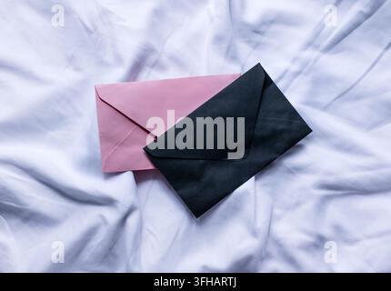 Black and pink envelopes lie on crumpled white fabric. The composition symbolizes a personal message, communication, and secrecy Stock Photo