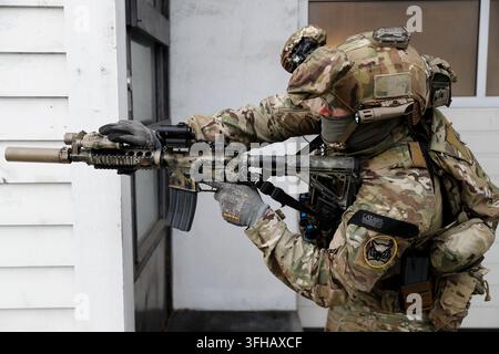 Tactical soldier (Forsvarets spesialkommando/FSK) in camouflage uniform aiming a rifle near building. Stock Photo