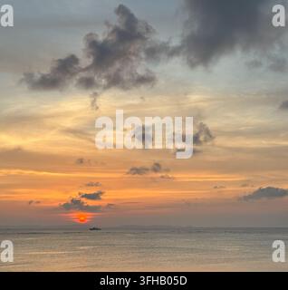Sunset over the ocean beneath dramatic clouds, with golden light ...