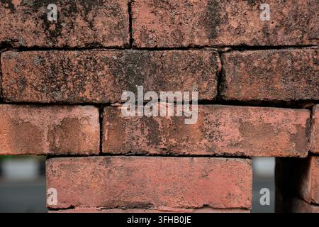 Close up of an old weathered red brick wall texture with dark stains, rough surface, and missing mortar revealing a gap. Stock Photo