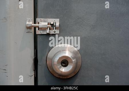 Close-up of a stainless steel door knob handle and sliding barrel bolt latch on a grey door. Stock Photo
