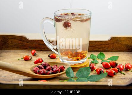 Making rose hip berry herbal tea, pouring boiling water over dried rose hip berries in a tea cup.Rose hip berries on wood spoon. Stock Photo