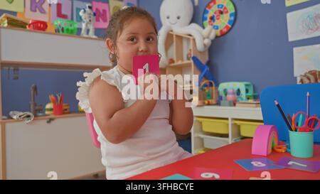 Girl arranging numbered cards on a table in a building preschool classroom with toys, scissors, pencils and colorful posters; concentration learning. Stock Photo