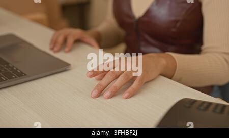 Woman hand hovering over light wood desk beside laptop in studio, fingers slightly splayed and poised above surface; focused productivity. Stock Photo