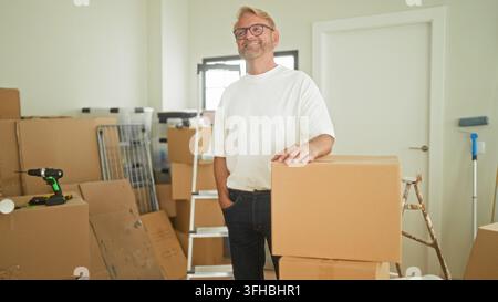 Man placing cardboard box with hand on top while steadying packages in a building; moving day contentment. Stock Photo