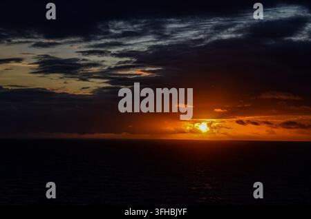 Dramatic orange sunset breaking through dark storm clouds over the open sea Stock Photo