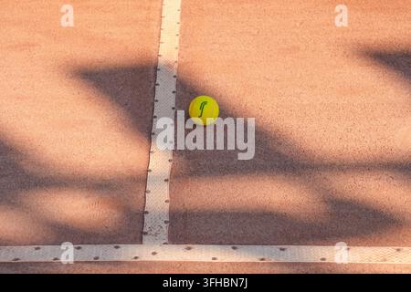 Yellow tennis ball on the court line with spotlight shadows. Stock Photo