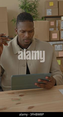 Man holds tablet and stylus, hand tapping screen and reviewing parcels on a packing table in building; focus organization. Stock Photo