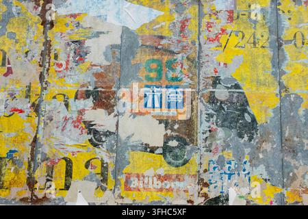 Weathered urban wall covered with torn posters, faded numbers and layered yellow, blue, grey and red paper textures Stock Photo