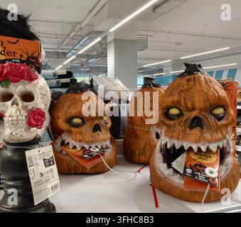 Pforzheim, Germany - September 16, 2026 Orange pumpkin skull figurines and one white skull with red roses sit on retail display tables inside bright s Stock Photo