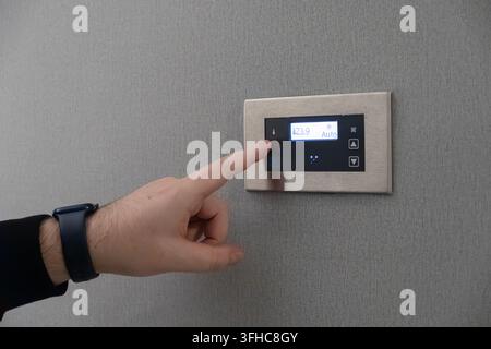 Person interacting with a modern touch screen temperature controller, demonstrating precise environmental management for residential heating or coolin Stock Photo