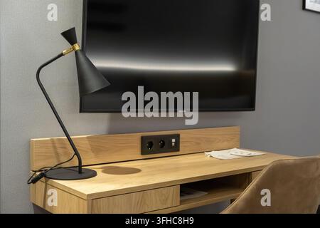 Modern oak desk featuring a stylish metal lamp and flat screen display on a grey wall, offering a clean environment for professional work or relaxatio Stock Photo