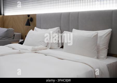 White linen pillows rest on a neat hotel bed with contemporary wood paneling and soft lighting, creating a calm atmosphere for rest in a stylish bouti Stock Photo