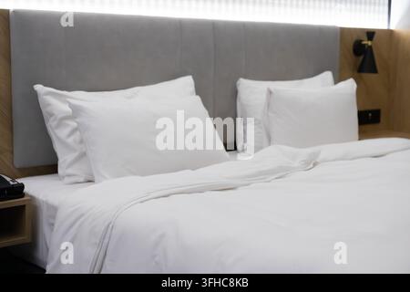 The minimalist hotel suite features a clean bed with soft bedding and ambient lighting, creating an inviting atmosphere designed for travel comfort, r Stock Photo