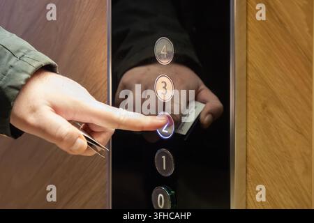 Close-up of a hand pressing an illuminated elevator button for floor two, holding an access card, emphasizing smart building technology and secure ent Stock Photo