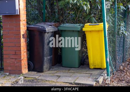 Black, green, and yellow household waste bins are neatly arranged on outdoor pavement by a brick pillar, highlighting effective waste sorting for urba Stock Photo