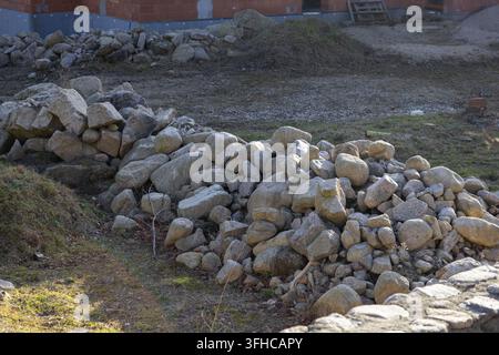 Abundant natural grey stones are meticulously piled on grassy ground at a building site, perfect for home renovation or modern landscaping projects Stock Photo