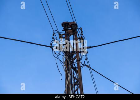 Close-up view of a decrepit electric utility pole with a densely packed, messy tangle of power lines, emphasizing urban infrastructure challenges and Stock Photo