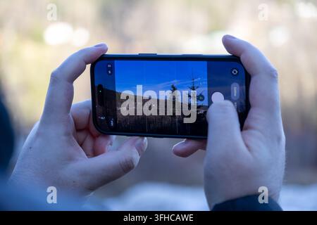 Hands holding a smartphone, actively capturing a beautiful outdoor landscape, displaying the camera app with PHOTO mode, ideal for travel, hobby, and Stock Photo