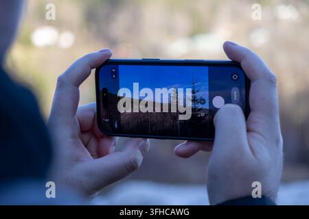A close-up of a person's hands holding a modern smartphone, framing a picturesque outdoor scene for a PHOTO, showcasing mobile photography and travel Stock Photo