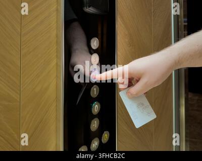 Close-up of human hand pressing illuminated second floor button in a modern elevator, holding a white key card, representing restricted access or hote Stock Photo
