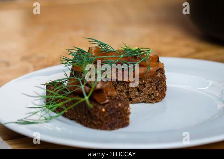 Cured ide fish on traditional dark rye bread, topped with tender orange fish pieces and fresh dill, served on a white plate. Stock Photo