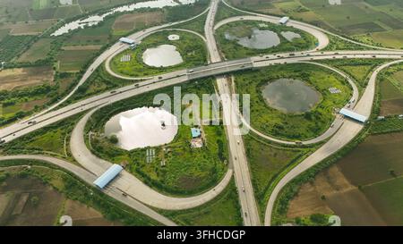 Aerial drone view of multi-level highway interchange with looping ramps and agricultural landscape near Dehgam, Gujarat, India Stock Photo