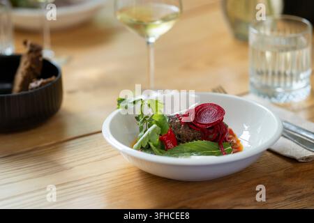 Beef patty served with vibrant pickled beetroot, fresh parsley and mint, red pepper and savory sauce in a white bowl. The beautifully plated meat dish Stock Photo