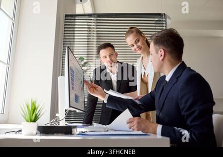 Colleagues discussing finance metrics on data dashboard at computer during meeting Stock Photo
