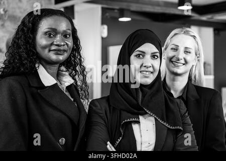Smiling business women with different ethnicities and cultures looking at camera in modern office - Three elegant female friends, one of them wearing Stock Photo