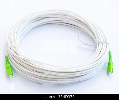 A white coiled fiber optic cable with green connectors lies on a white surface Stock Photo