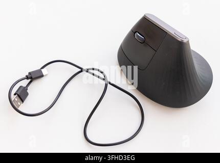 A black ergonomic vertical mouse and its USB cable rest on white Stock Photo