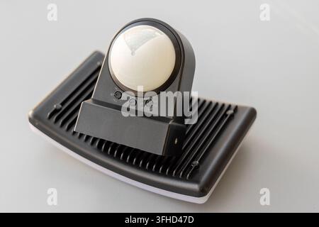 A black motion sensor LED floodlight sits on a plain white surface Stock Photo