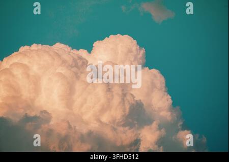 Large fluffy cumulus cloud formation glowing in warm light against a deep blue sky. Stock Photo
