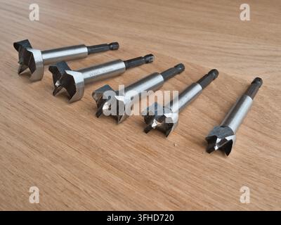 Five Forstner Drill Bits on Wood Surface - Set of five steel Forstner drill bits arranged on a light oak wooden surface, varying sizes for woodworking Stock Photo