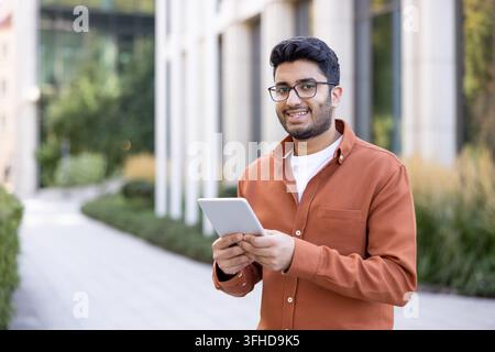 Digital nomad lifestyle and remote work, young man using a tablet for business communication in an urban office park. Professional connectivity and mobile technology. Stock Photo